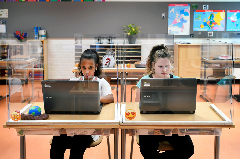 Dos alumnas en una escuela en Países Bajos, con plexiglass alrededor de sus pupitres.
