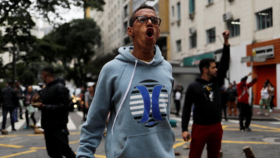 Протестующий кричит против полиции, блокируя дорогу в Сан-Паулу