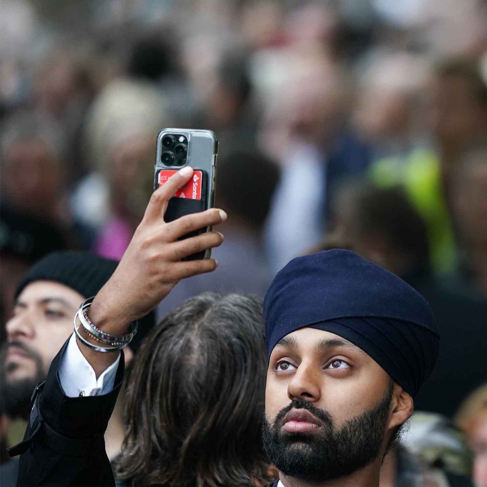 A man holds his phone up to capture the procession as it passes him