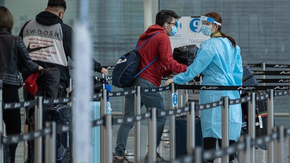 香港國際機場入境大堂內一名身穿醫療防護裝備的女工作人員（右）引領入境旅客排隊接受初步檢疫檢測（27/10/2021）