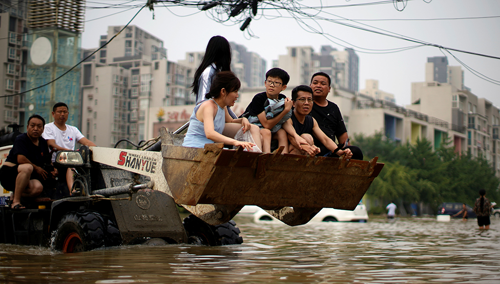 Cuatro personas viajan en un cargador frontal mientras atraviesan las inundaciones tras las fuertes lluvias en Zhengzhou, provincia de Henan, en China, el 23 de julio de 2021