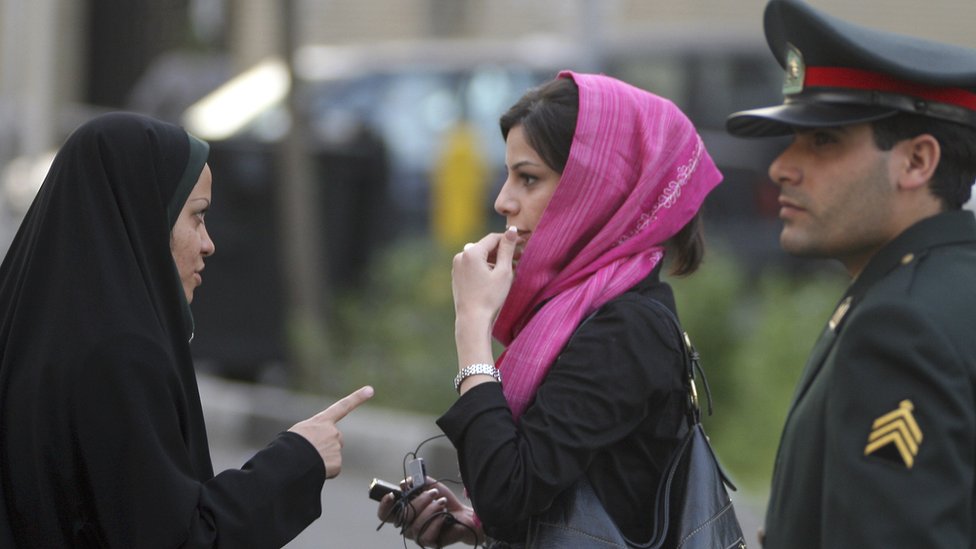 Член иранского патруля морали (l) в Тегеране в апреле 2007 года упрекает молодую женщину (c) за ее платье.
