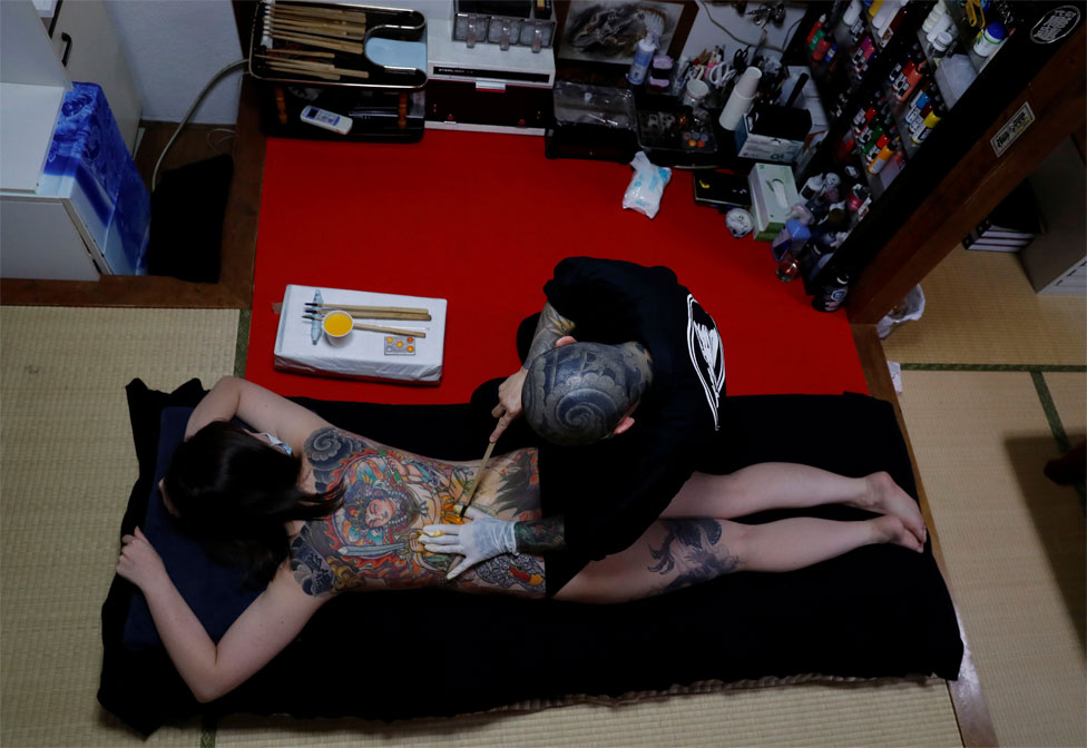 Тату-мастер делает татуировку на спине женщины в своей студии
