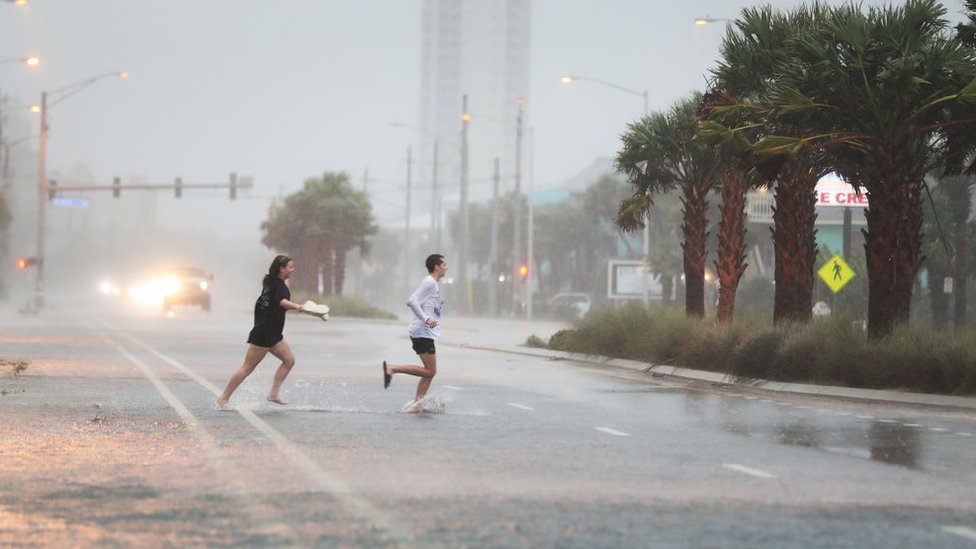 Люди перебегают дорогу сквозь дождь и ветер, когда внешние полосы урагана Салли выходят на берег 15 сентября 2020 года в Галф-Шорс, Алабама