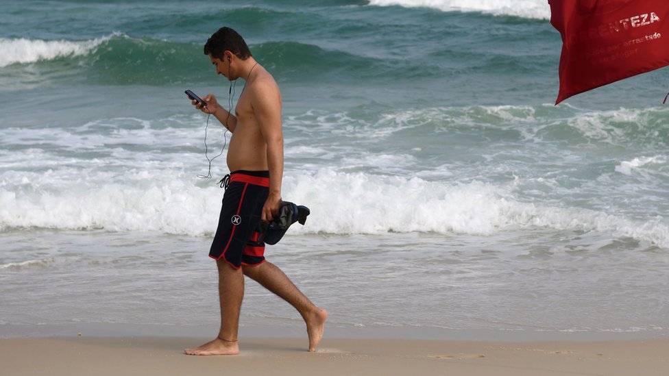 man checking phone while walking down the beach in Brazil