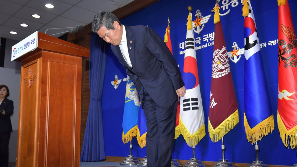 Министр обороны Южной Кореи Чон Кён Ду кланяется перед корейскими флагами на июньской пресс-конференции, на которой он принес извинения гражданам за вторжение рыбацкой лодки