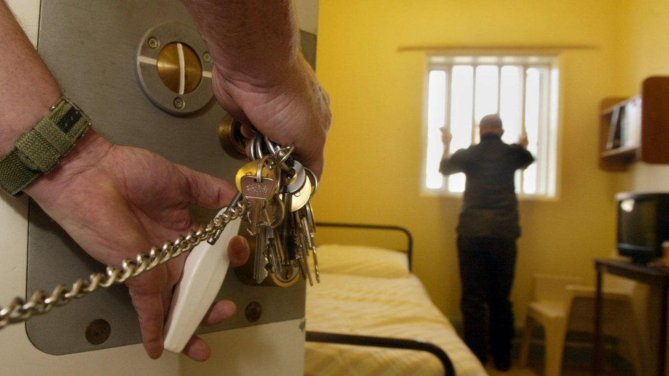 Un preso sin identificar mira por la ventana mientras un funcionario de prisiones se dispone a cerrar la celda