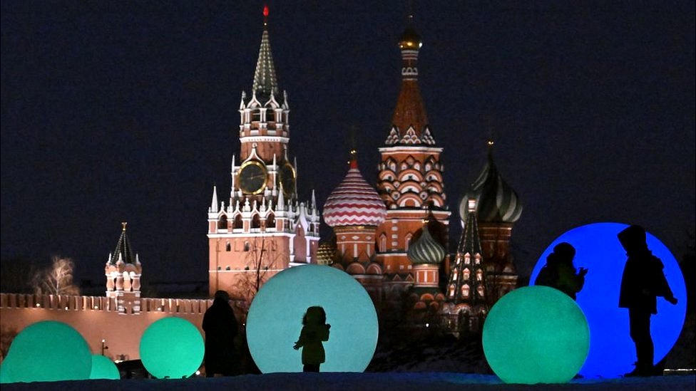 People walk past light installations at Zaryadie park in front of the Spasskaya tower of the Kremlin (L) and the Saint Basil cathedral (R), in Moscow on February 19, 2023.