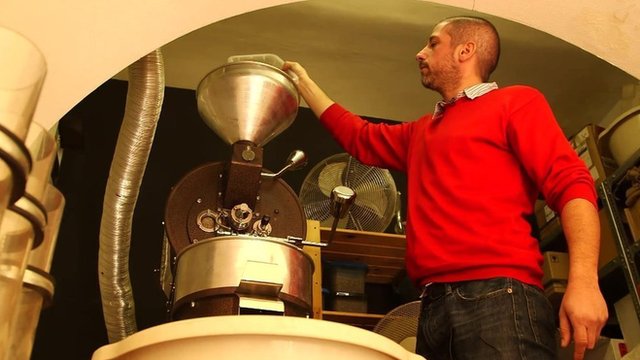 Peter Laszlo pours coffee beans into his roaster in his Budapest cafe, Lumen