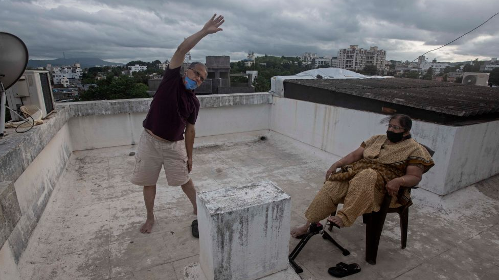 Um homem idoso se exercita em um telhado ao lado de sua esposa em Nova Delhi