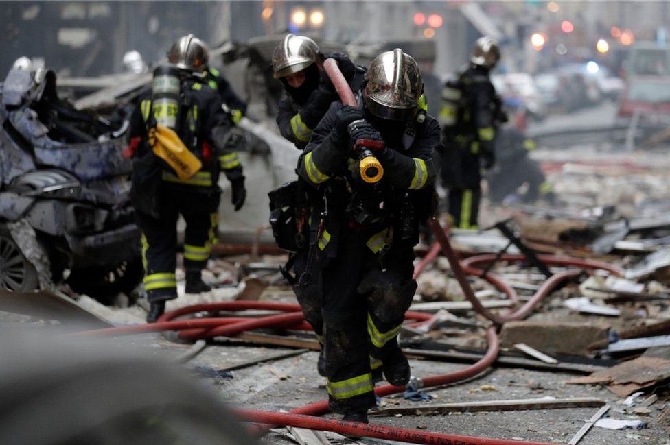French firefighters in helmets run with a hose near a Paris bakery on the corner of the streets Saint-Cecile and Rue de Trevise