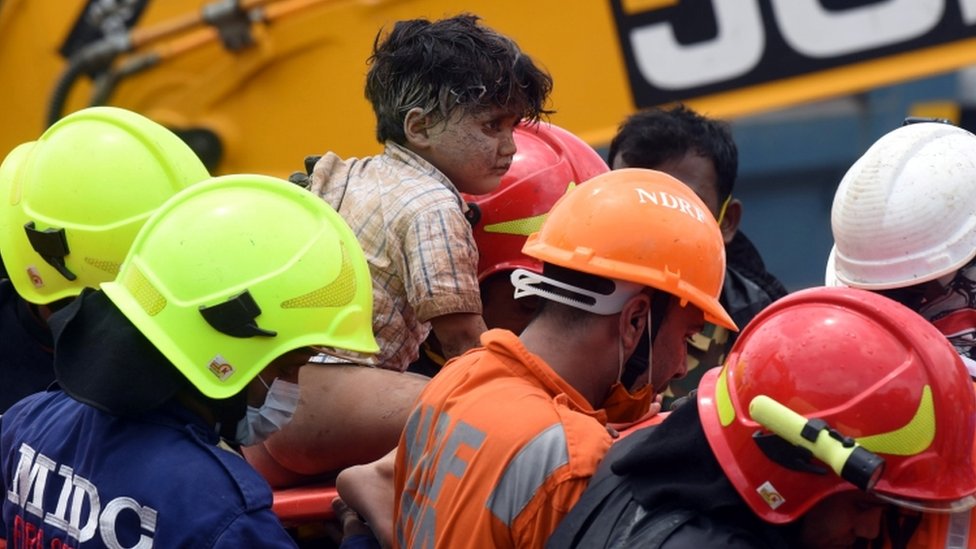Спасатели несут Мохаммеда Банги, четырехлетнего мальчика, после того, как его спасли из-под завалов на месте обрушившегося пятиэтажного здания в Махаде