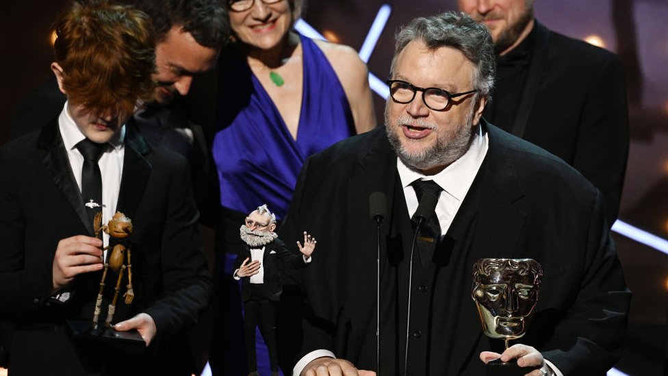 Guillermo del Toro y parte del elenco de "Pinocho" durante la entrega del Premio Bafta junto a los muñecos de Gepetto y Pinocho que aparecen en la cinta.