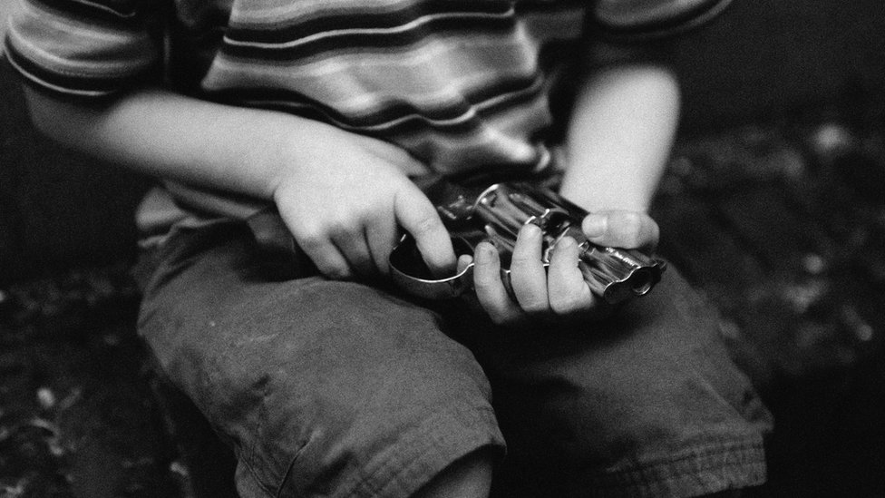 Un niño sostiene un revolver en sus manos