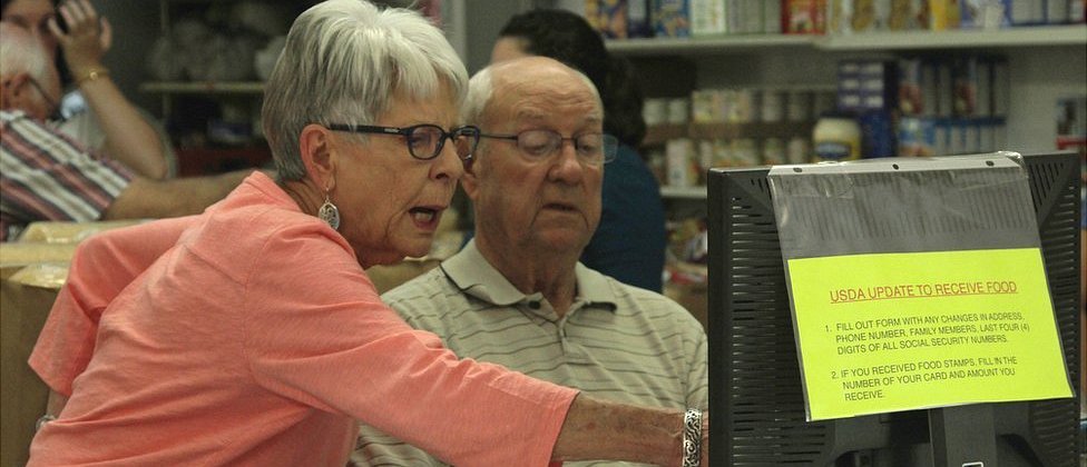 "Es una lástima que tengamos que imponer la veda de seis semanas", dice Frogge. Y la vemos poner en práctica las reglas apenas un instante más tarde: dos jóvenes vienen en busca de su caja, pero un rápido control en los registros revela que no se ha cumplido el plazo... y se van con las manos vacías. Sally Frogge frente a una computadora en el banco de alimentos, Jamestown