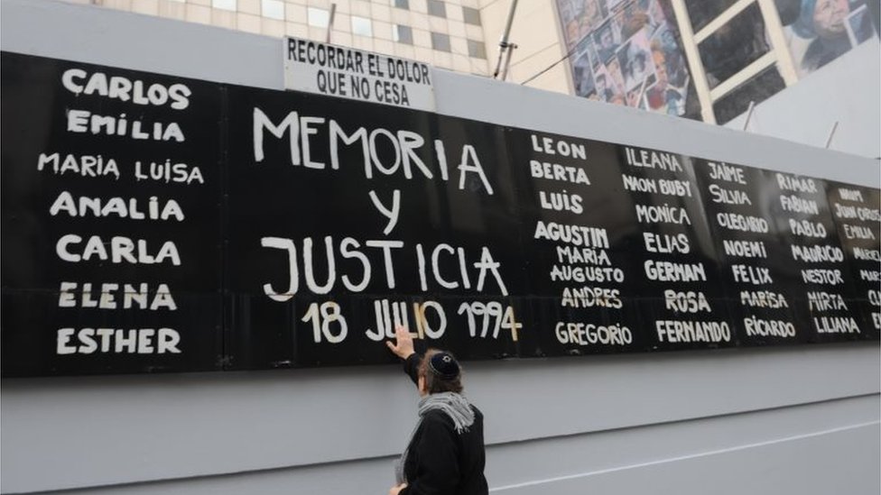 Мужчина дотрагивается до рекламного щита с именами жертв во время мероприятия, посвященного 25-летию нападения на организацию Asociacion Mutual Israelita Argentina (AMIA), в Буэнос-Айресе, Аргентина, 18 июля 2019 г.