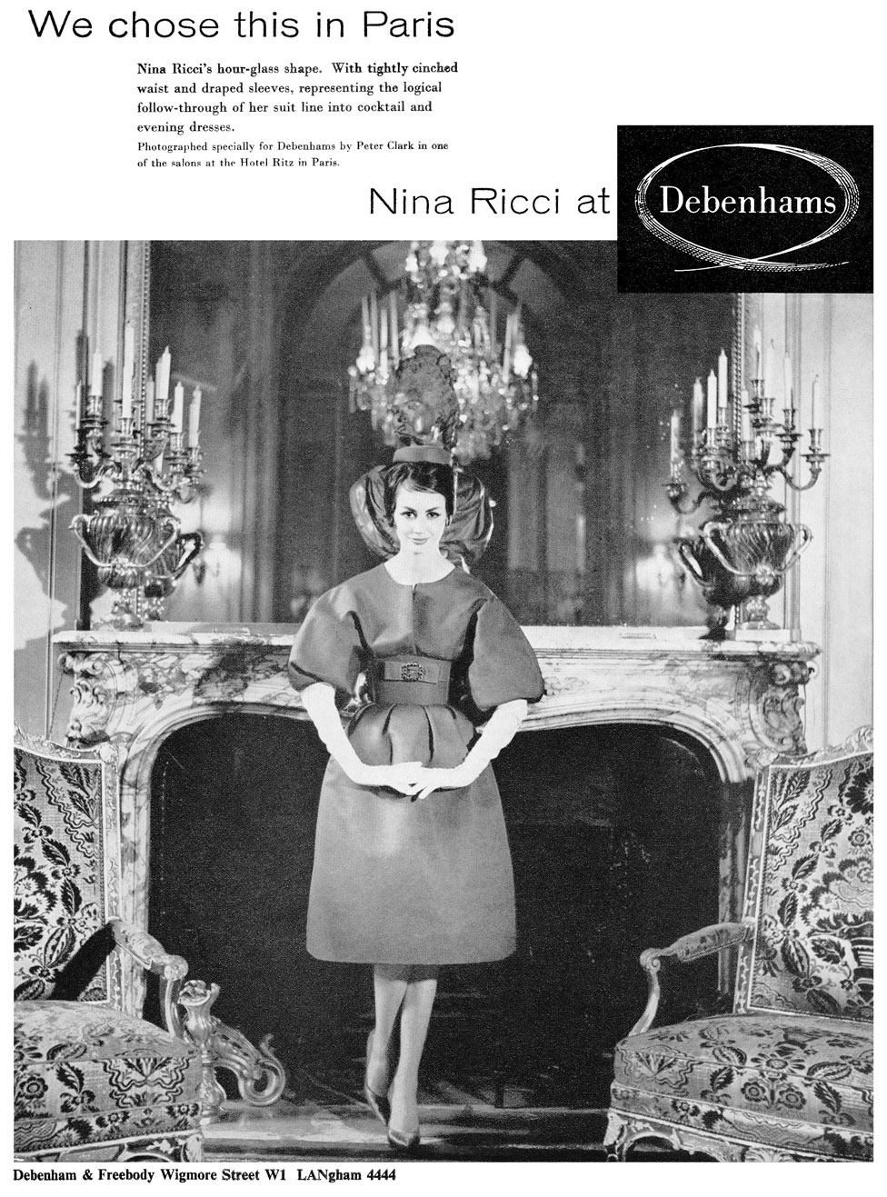 Реклама модного бренда, изображающая женщину в платье, стоящую перед элегантным камином