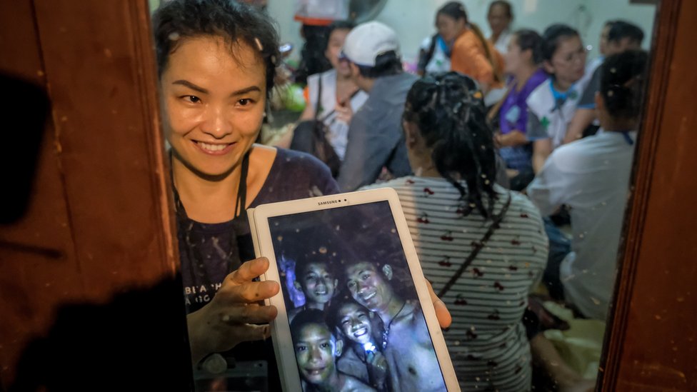 Una mujer sostiene una tablet con la foto de niños atrapados en Tailandia