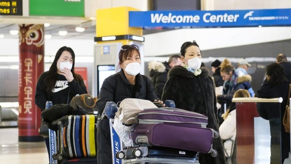 Посетители в медицинских масках прибывают в аэропорт Нью-Йорка JFK