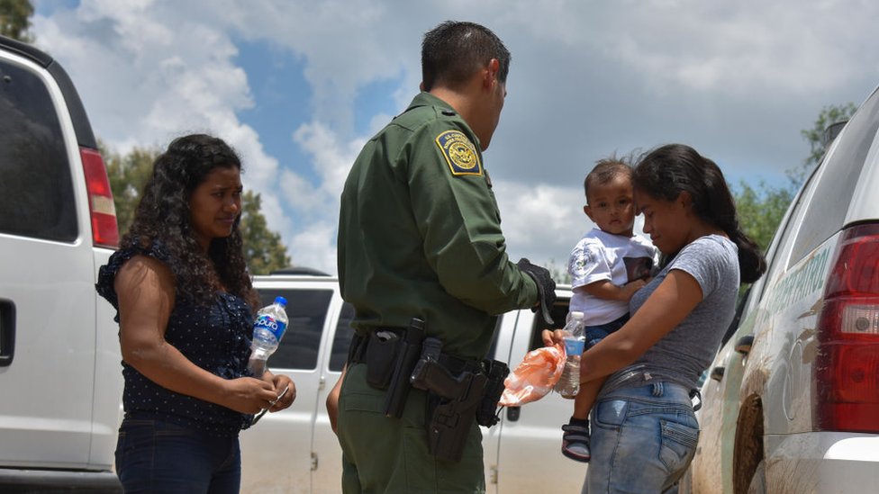 Una madre indocumentada con su hijo en brazos con un agente fronterizo de los EE.UU.