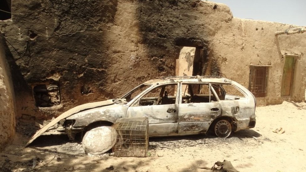 A burned out car next to a badly burned building