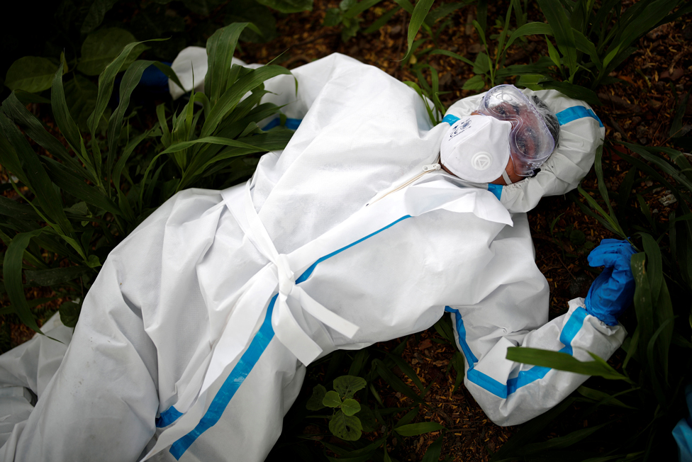 A health worker wearing protective clothing rests on the ground in India