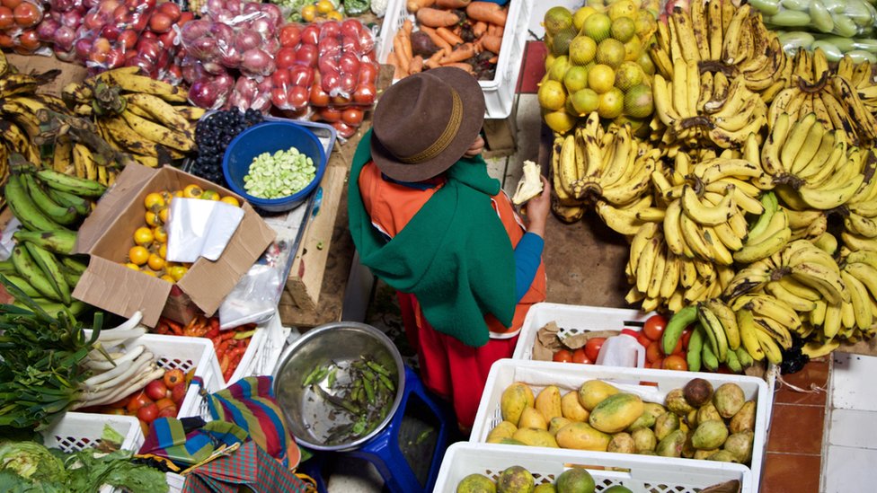 Persona rodeada de alimentos en un mercado de Perú.