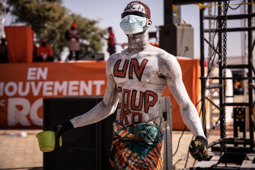 A man walks at a rally with the words "un coup KO", meaning "a knockout blow", painted on his torso.