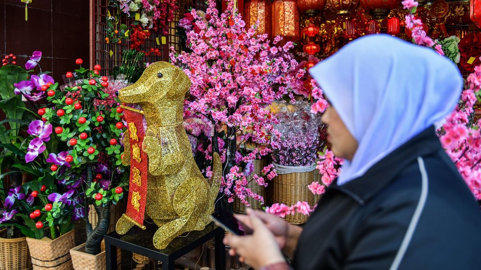 Мусульманка проходит мимо золотой статуи собаки перед празднованием Лунного Нового года в китайском квартале Куала-Лумпура