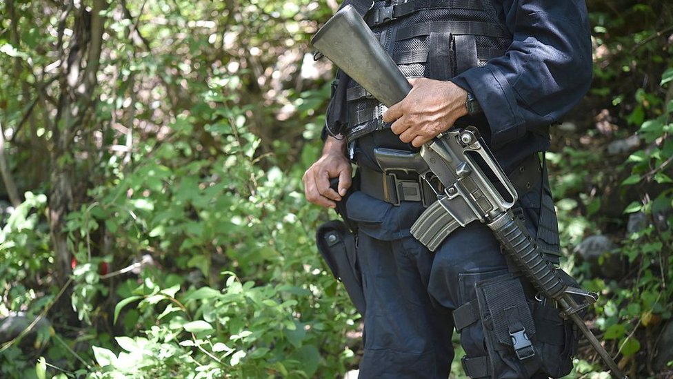 Algunos policías en México son parte de la corrupción que permite que algunos crímenes queden impunes, señalan expertos. Un policía mexicano parado con un fusil cerca de una fosa común.