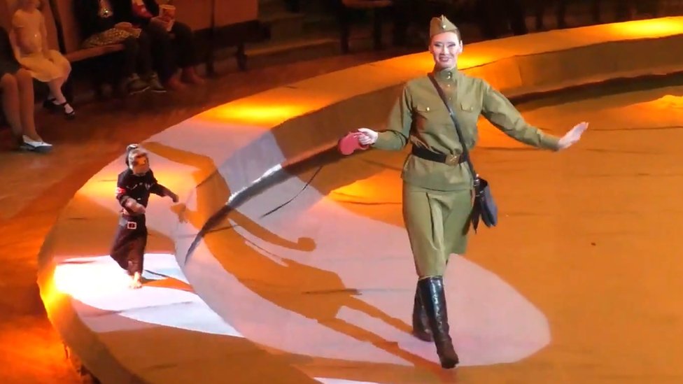 Circus performance featuring a woman in uniform and a monkey on a leash