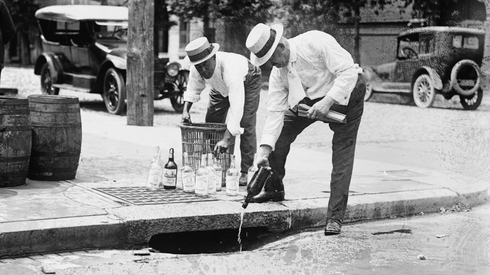 Agentes derraman alcohol incautado por una alcantarilla, cerca de 1921