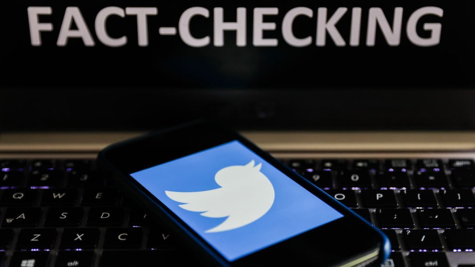 Imagen de un letrero sobre verificaciión de datos junto a un celular con una imagen de Twitter.
