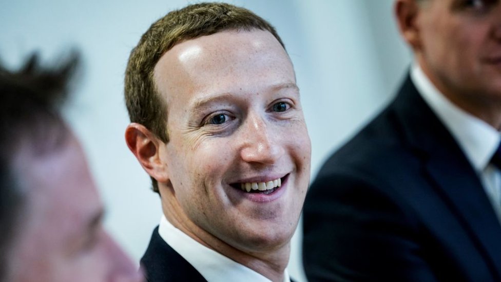 Facebook founder Mark Zuckerberg smiles at the camera in this close-up shot of a group, with other members obscured by the framing