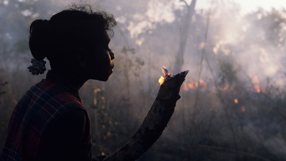 A girl in Arnhem Land, Australia, holds a small branch which flickers with flame
