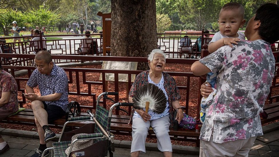 Пожилая китаянка смеется вместе с мужчиной, несущим ребенка, в парке Ритан 10 июня 2016 года в Пекине, Китай.