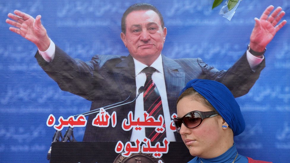 إحدى مؤيدات مبارك أمام ملصق تأييد له في عيد ميلاده خارج المستشفى حيث كان يعالج