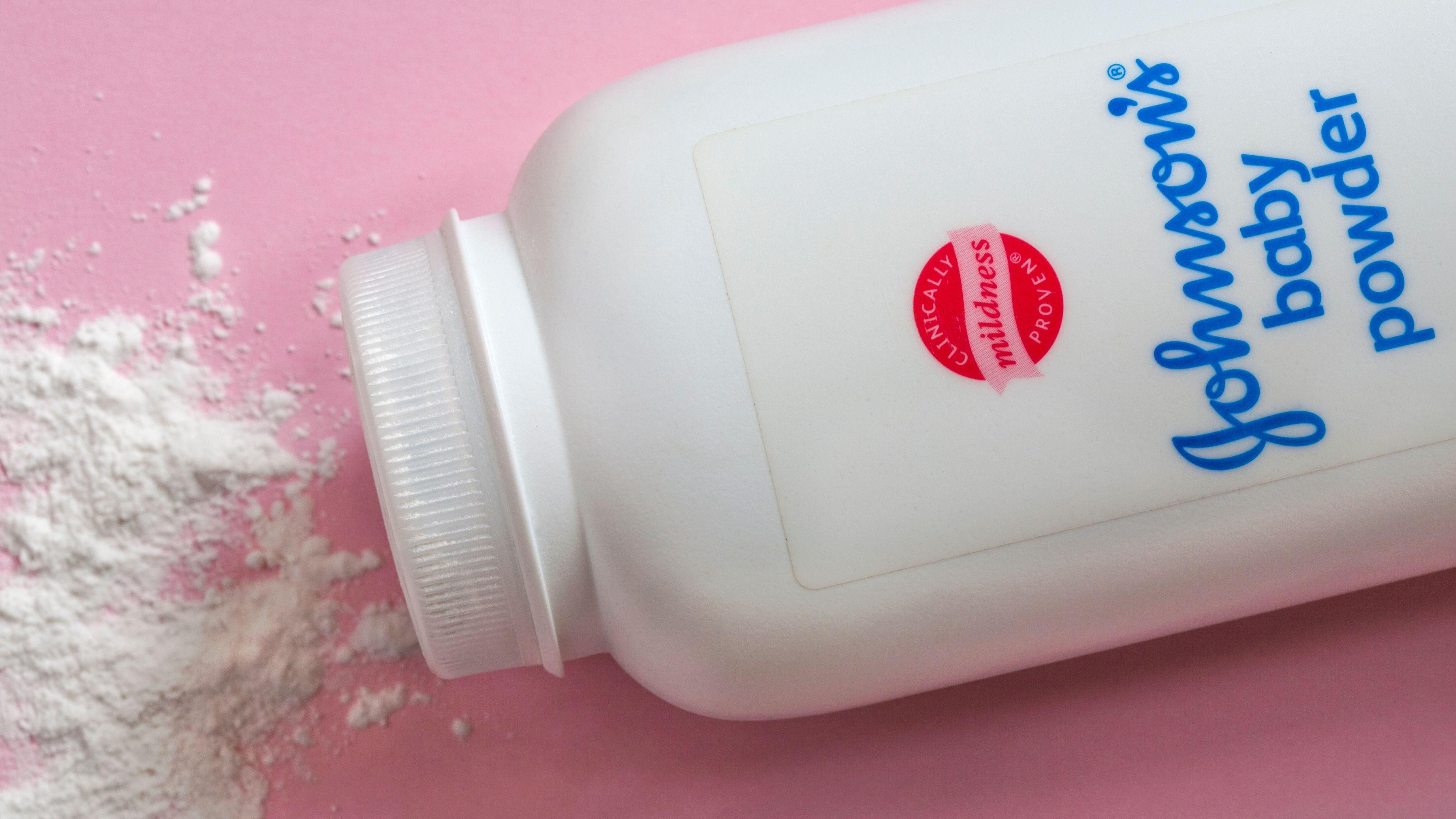 Partially opened container of Johnson's Baby Powder with some powder spilled around it on a soft pink surface