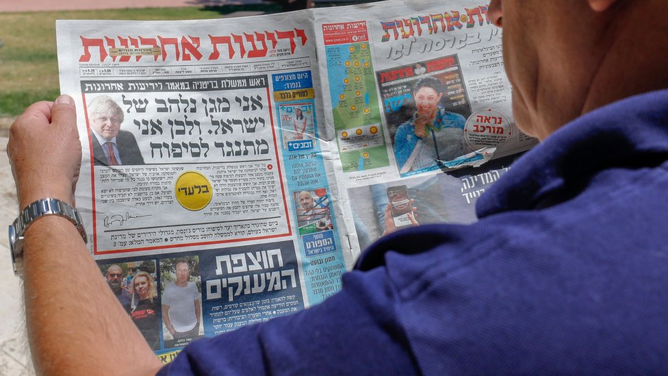 Мужчина смотрит на статью Бориса Джонсона на первой полосе израильской газеты на иврите Yedioth Ahronoth (1 июля 2020 г.)