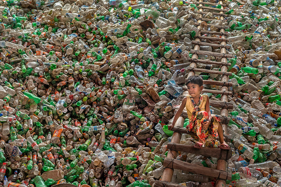 Un menor sentado en una escalera, rodeado de botellas de plástico destinadas a una fábrica de reciclaje en Chittagong, Bangladesh