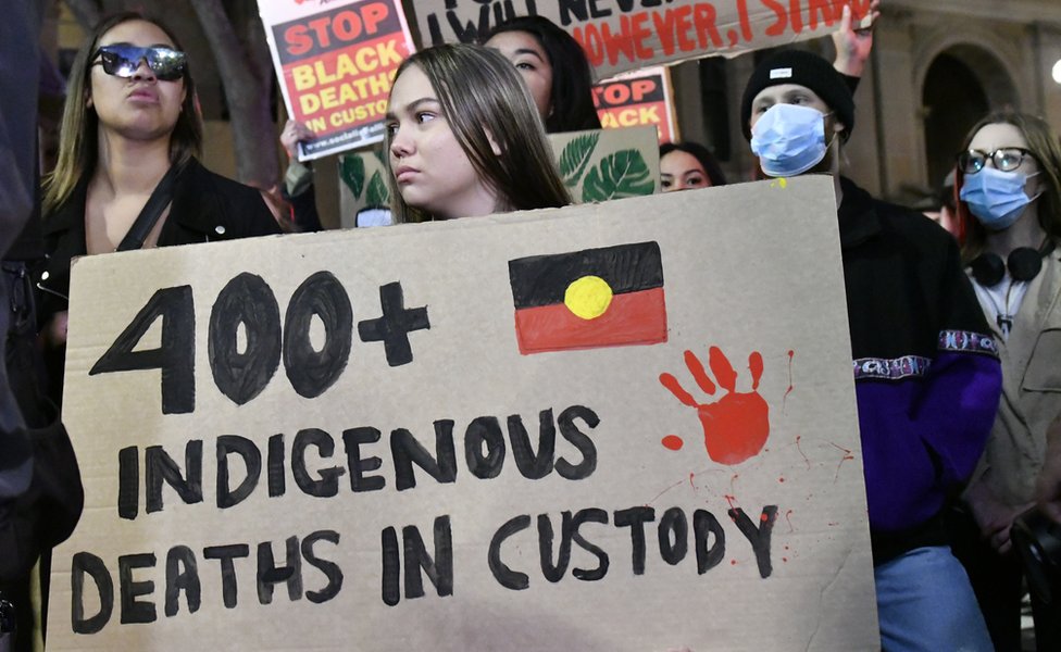 Протестующий на марше «Black Lives Matter» в Сиднее держит табличку с надписью «400 смертей коренных народов в заключении»