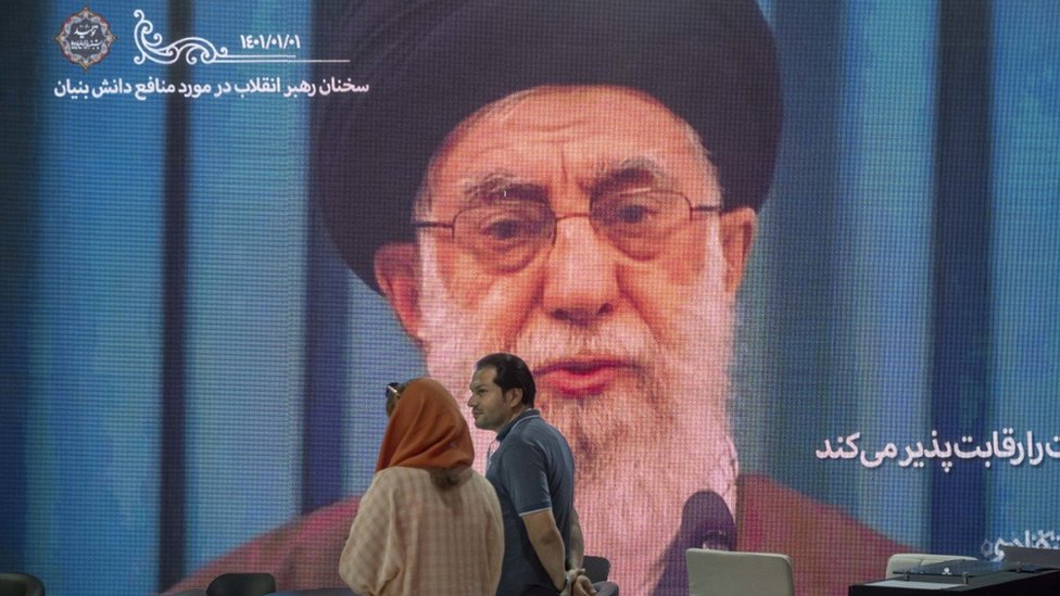 Dos personas frente a un retrato gigante del líder supremo de Irán, Alí Jamenei.