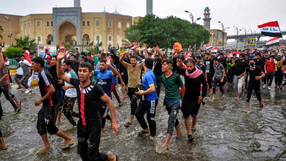 Антиправительственные демонстранты маршируют по паводковым водам в городе Наджаф