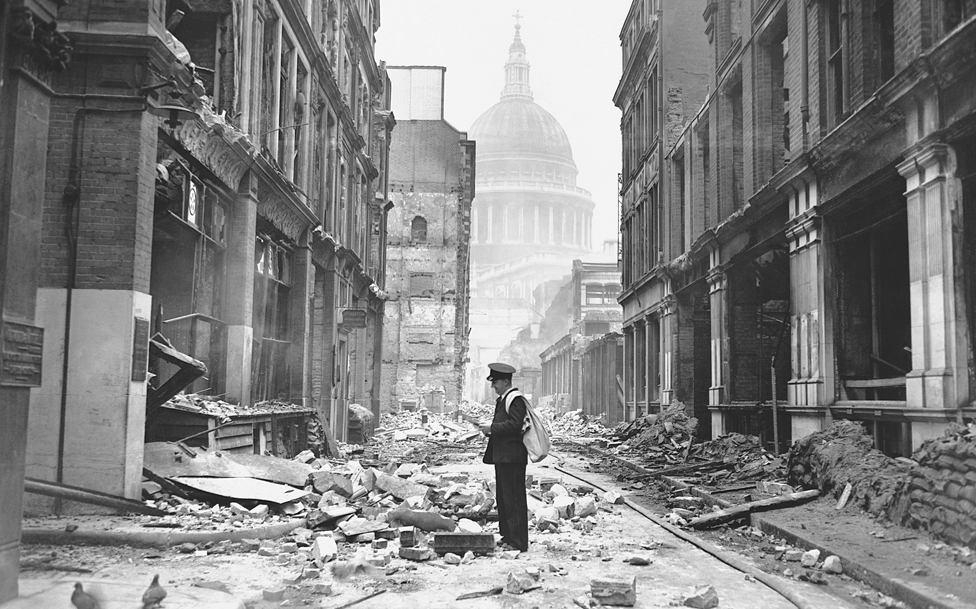 A postman attempting to deliver letters in a bomb-damaged street near Paul's Cathedral at the end of the London Blitz, May 1941