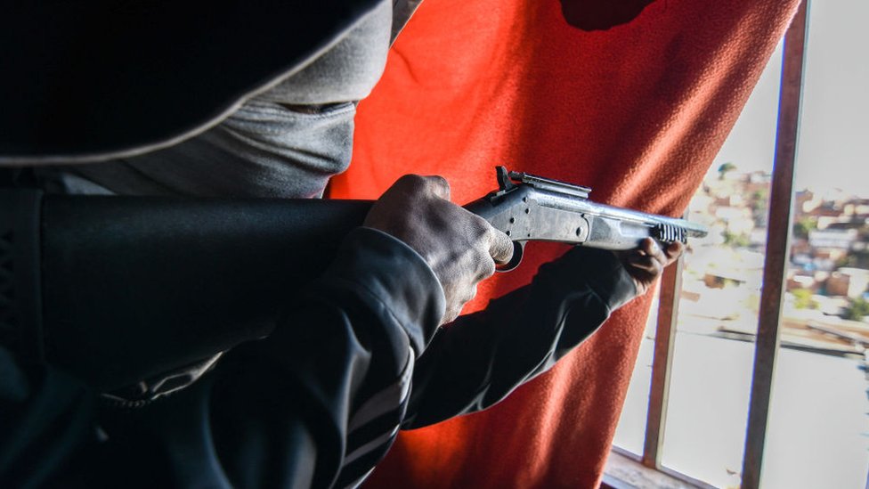 Un hombre sostiene una escopeta frente a una ventana en un barrio de Caracas.