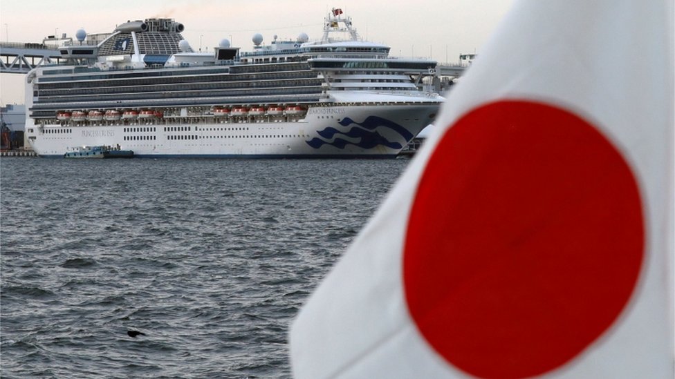 The cruise ship Diamond Princess is seen beside a Japanese flag as it lies at anchor while workers and officers prepare to transfer passengers tested positive for the novel coronavirus, at Daikoku Pier Cruise Terminal in Yokohama, south of Tokyo, Japan February 12, 2020