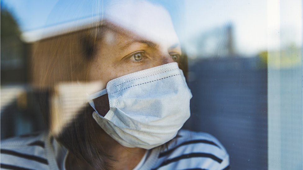 woman wearing mask looking out of window