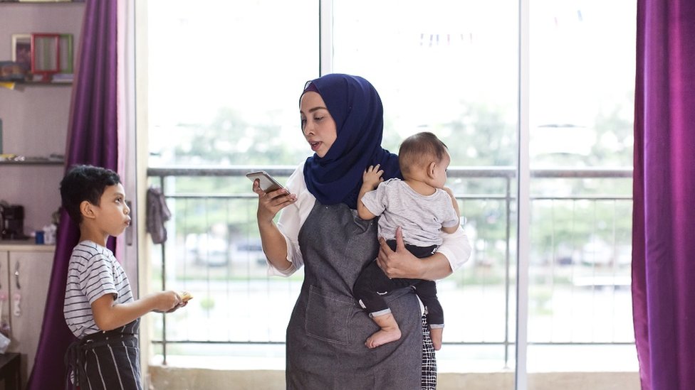 Una madre multitarea con teléfono inteligente y niños