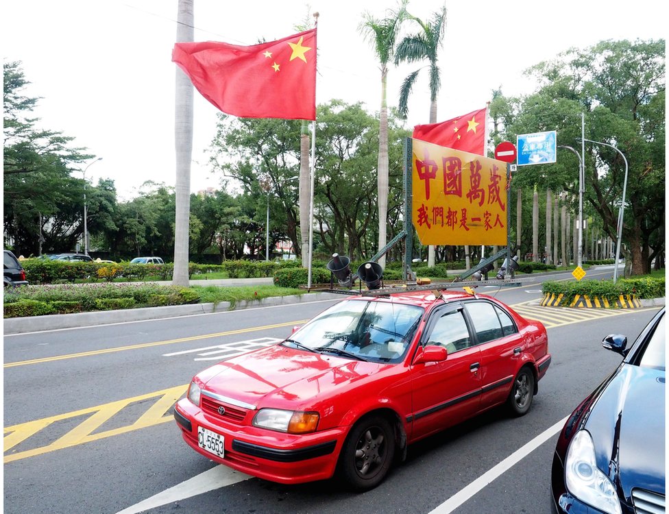 Член группы сторонников объединения водит красную машину с национальными флагами Китая и надписью «Да здравствует Китай. Мы - одна семья», чтобы выразить поддержку предстоящей встрече между президентом Тайваня Ма Ин-цзю и Председатель Китая Си Цзиньпин, Тайбэй, Тайвань, 4 ноября 2015 г.