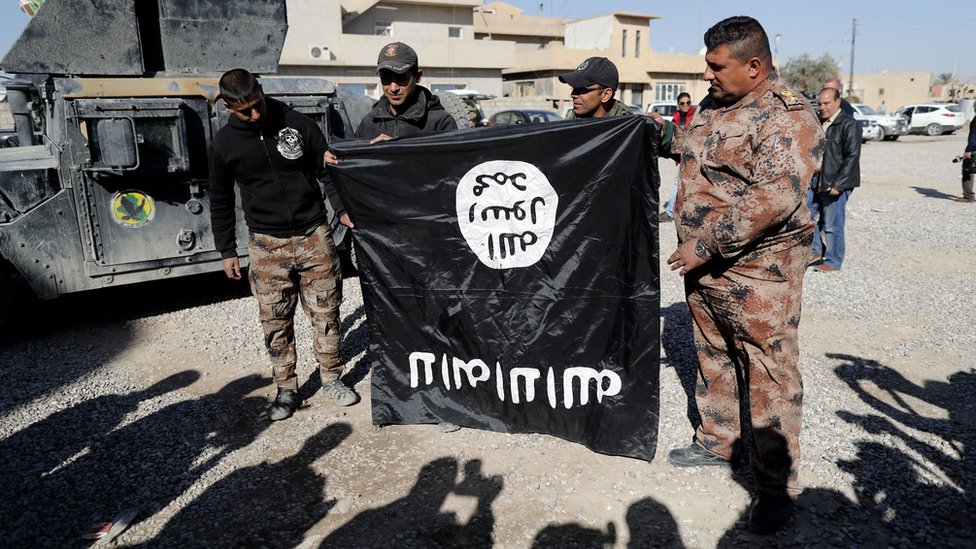 Iraqi army soldiers hold a flag from the Islamic State (IS) jihadist group up-side-down on November 23, 2016, near an Iraqi army base in the outskirts of Mosul. Forces battling the Islamic State group in northern Iraq cut off the jihadists' last supply line from Mosul to Syria, trapping them in the city for a bloody last stand. (Photo by THOMAS COEX / AFP) (Photo by THOMAS COEX/AFP via Getty Images)